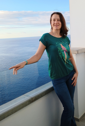 Elvira steht auf einem Balkon mit Blick  auf das Meer